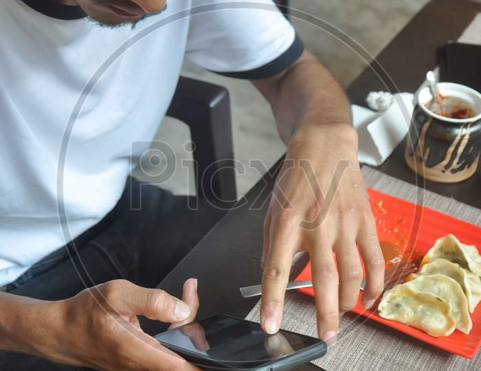 High angle view of a young guy using phone during eating fast food in the cafe