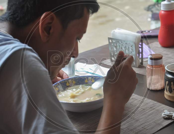 A asian young guy eating thenthuk (tibetan cousin) in tibetan cafe