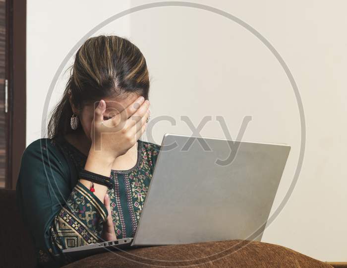 Young Indian Working Girl Feeling Headache While Working On Her Laptop.Eeling Desperate Alone At Home. Unhappy Stressed Millennial Indian Ethnicity Woman Hiding Face In Hands, Suffering From Life Problems Or Headache.