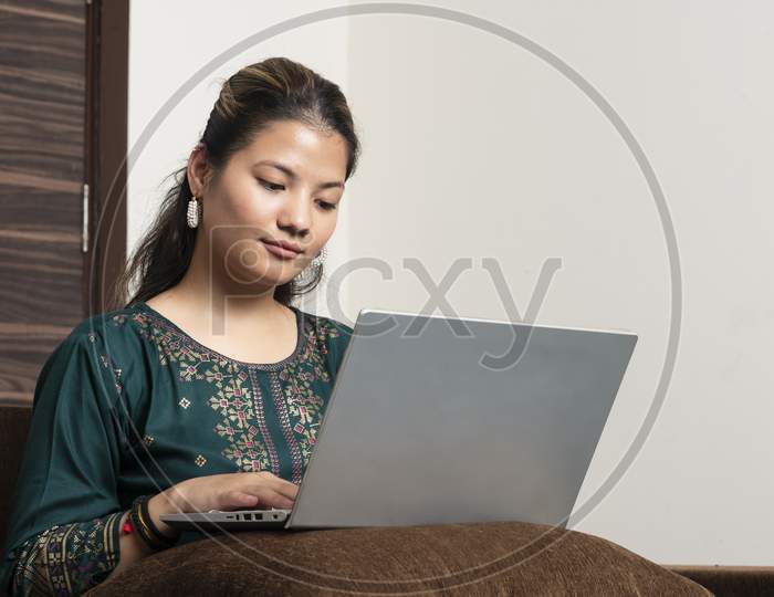Young Indian Ethnic Girl Student Freelancer Working From Home While Sitting On The Couch, Looking At Pc Screen Focused On Thinking And Solving Online Problem.