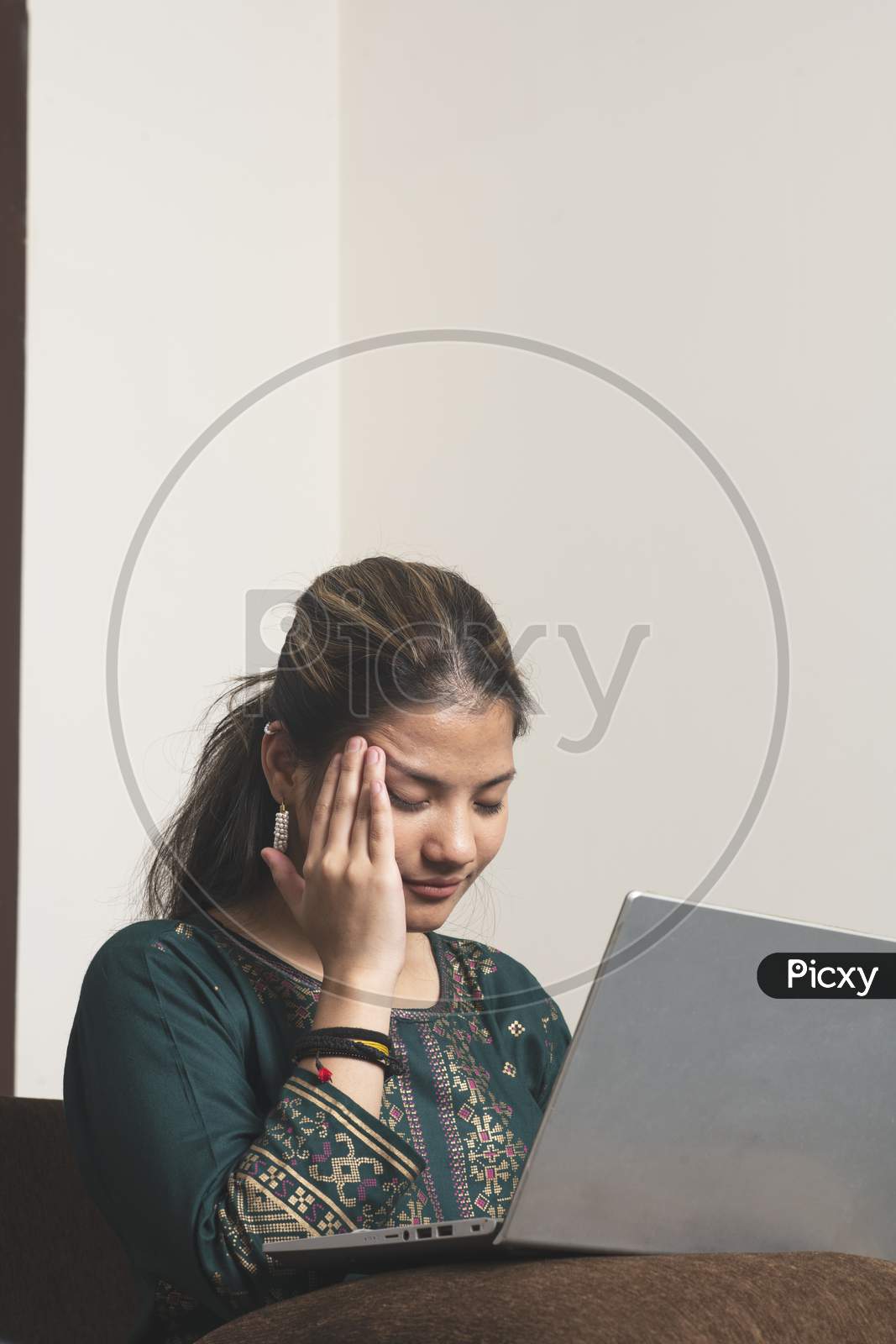 Young Indian Working Girl Feeling Headache While Working On Her Laptop.Eeling Desperate Alone At Home. Unhappy Stressed Millennial Indian Ethnicity Woman Hiding Face In Hands, Suffering From Life Problems Or Headache.