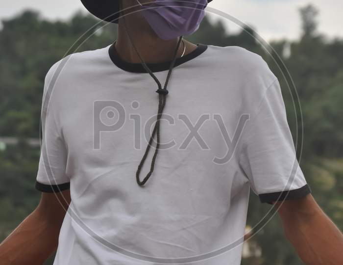 A Indian young man standing outside with wearing boonie hat, white t-shirt and face mask during coronavirus pandemic with looking at camera