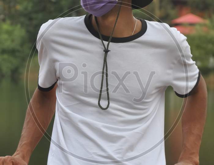 A Indian young man standing outside with wearing boonie hat, white t-shirt and face mask during coronavirus pandemic with looking at camera