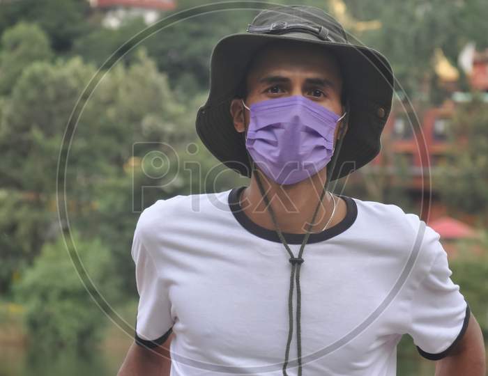 Close-up of a young man standing outside with wearing boonie hat and face mask during covid19 with looking at camera