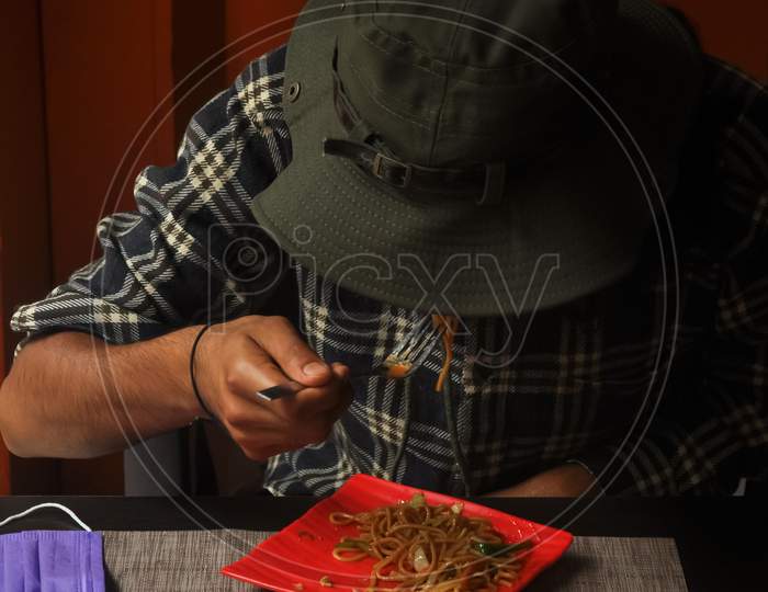 A man with wearing boonie hat eating noodles in the cafe during coronavirus pandemic