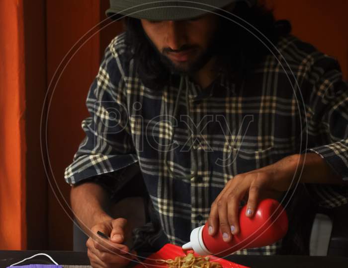 A bearded and long haired young man eating noodles in the restaurant during Covid-19 pandemic. A man with wearing boonie hat during eating fast food