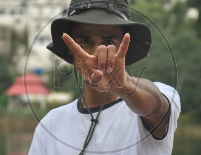 Close-up shot of a good young man showing rock sign with his hand with wearing hat and white t-shirt and looking at camera