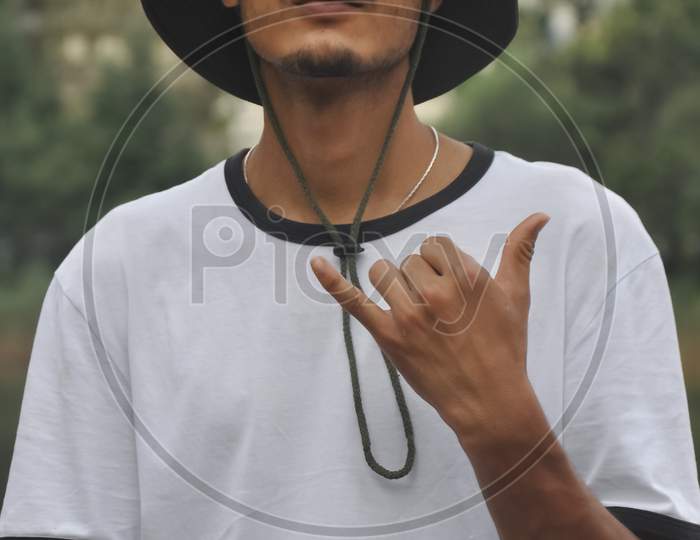 Portrait of a good looking Indian young guy making shaka sign with his hand with wearing hat and white tshirt and looking at camera