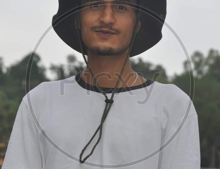 Close-up front view of a Indian young guy standing outdoor with wearing boonie hat and white tshirt and looking at camera
