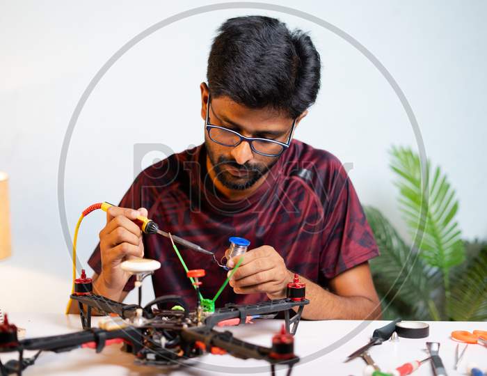 Young Man Or Student Making Drone By Soldering Wires To Baord At Home - Concept Of Drone Repair And Develoment, Scientific Experimenting Or Researching.