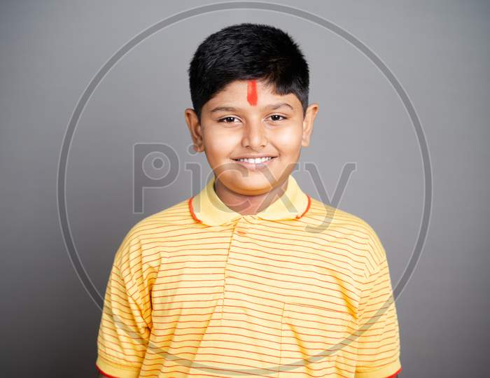 Happy Hindu kid with kumkum Bindi or Tilak on forehead by looking at camera on studio background - concept of smiling and positive joyful expression.