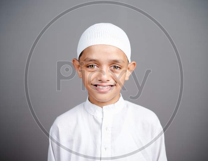 Smiling Muslim Child With Traditional Cap By Looking At Camera On Gray Background - Concept Showing Of Happiness, Positive Emotion During Childhood