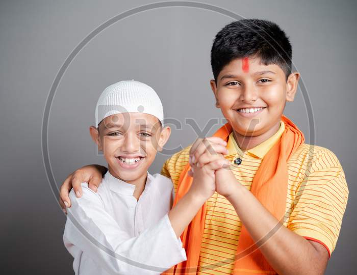 Happy Hindu Muslim Kids Showing Unity By Holding Hands Together By Looking At Camera On Gray Background - Concept Of Diversity, Bonding And Multiethnic Friendship.