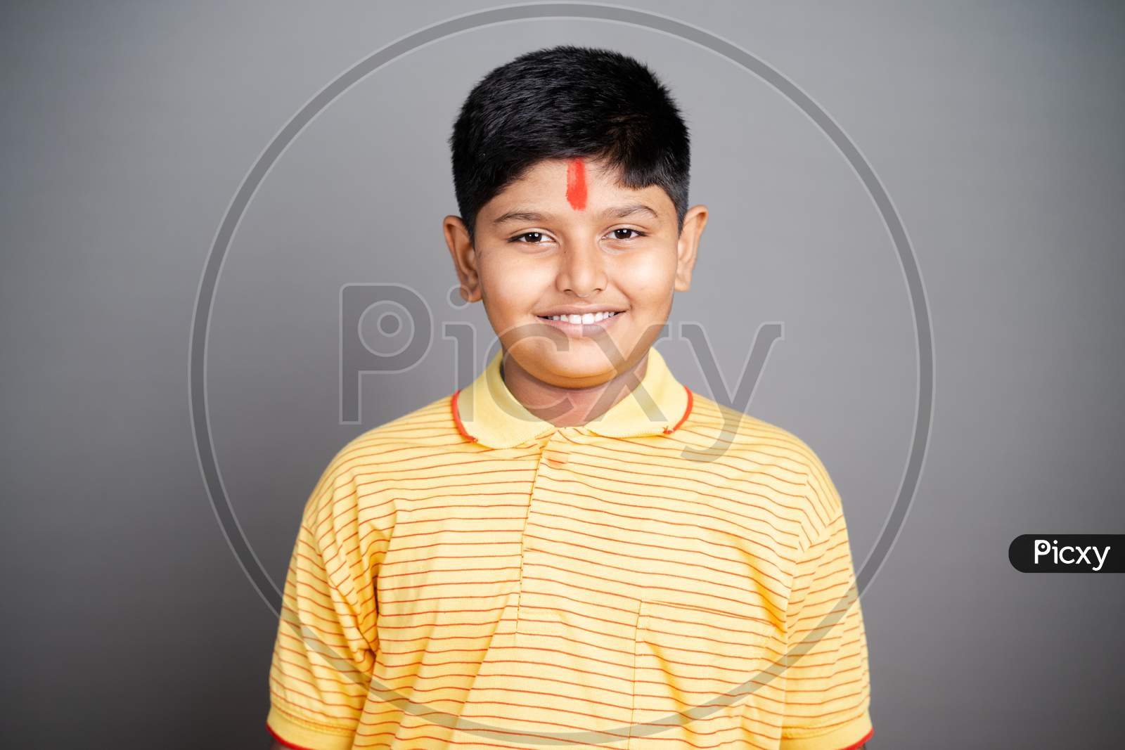 Happy Hindu kid with kumkum Bindi or Tilak on forehead by looking at camera on studio background - concept of smiling and positive joyful expression.