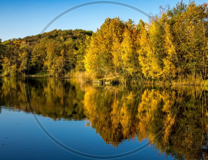 A beautiful little lake called Oberwaldsee in Germany at a sunny day in Autumn with a colorful forest reflecting in the water.