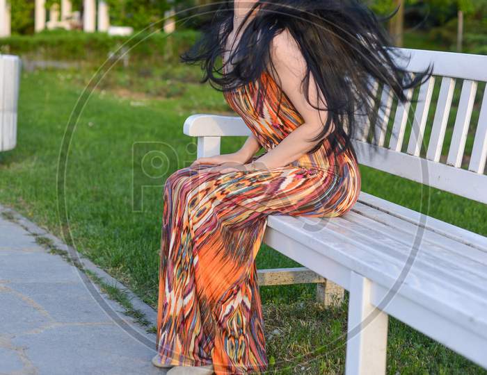 Beautiful Brunette Model With Long Hair Is Having A Photo Shooting In The Park. The Woman Is Wearing An Orange Long Summer Dress