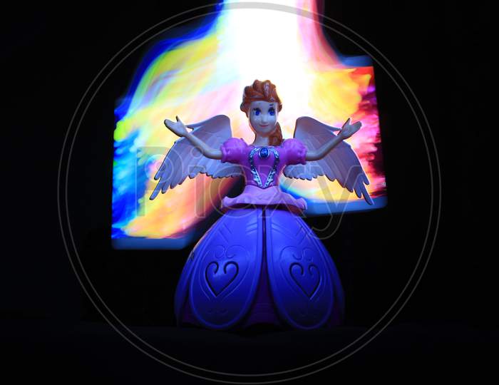Colorful Light Painting In Front And Behind The Beautiful Angel Doll On The Black Background