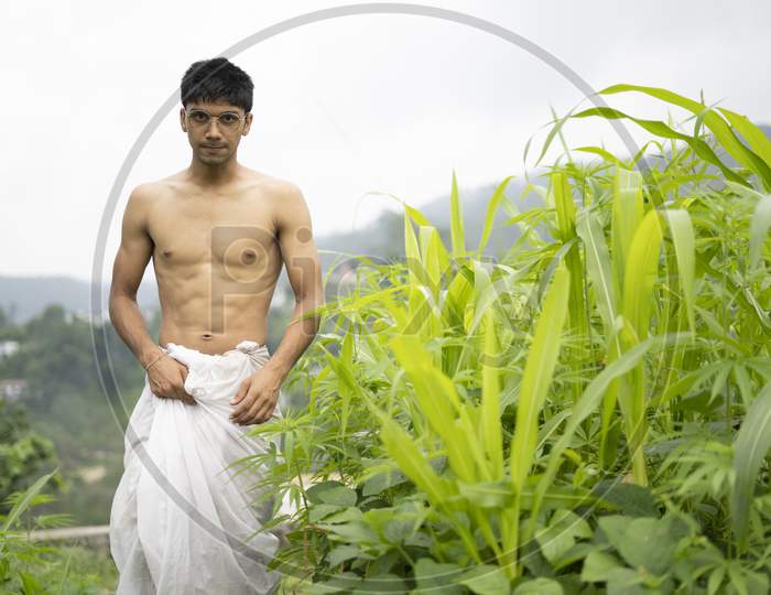 Young Indian Fit Boy, Walking On A Pathway Beside Crops In The Field. An Indian Priest Walking While Wearing White Dhoti. Indian Religious Man.