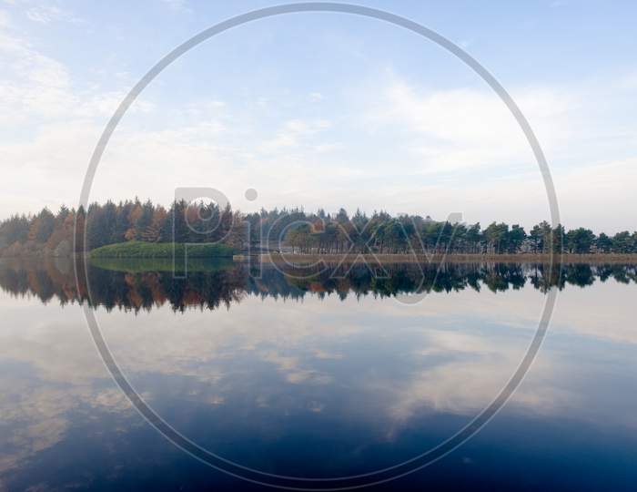 Wide Angle Autumn Season Forest Reflected In Calm Reservoir Water