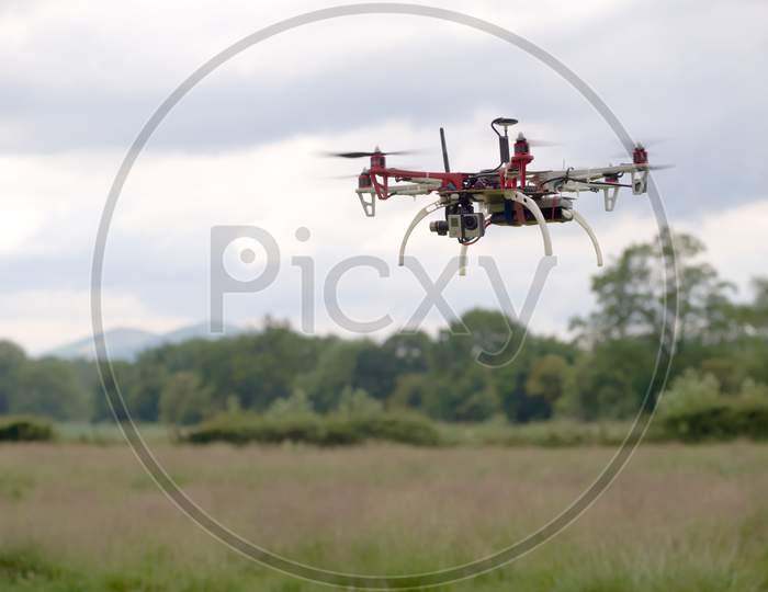 Hex Copter Camera Drone Hovers In Front Of A Rural Background.