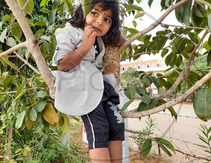 Closeup Of Young Indian Girl Kid Sitting Above The Branch Of A Tree.
