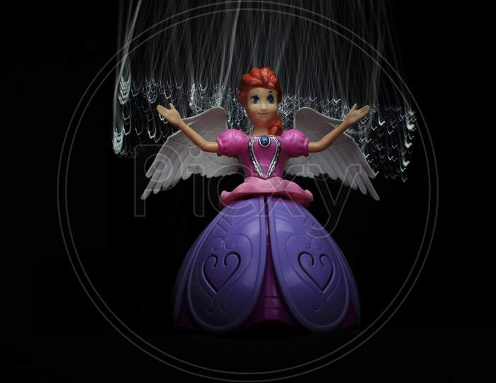 Colorful Light Painting Infront And Behind The Beautiful Angel Doll On The Black Background