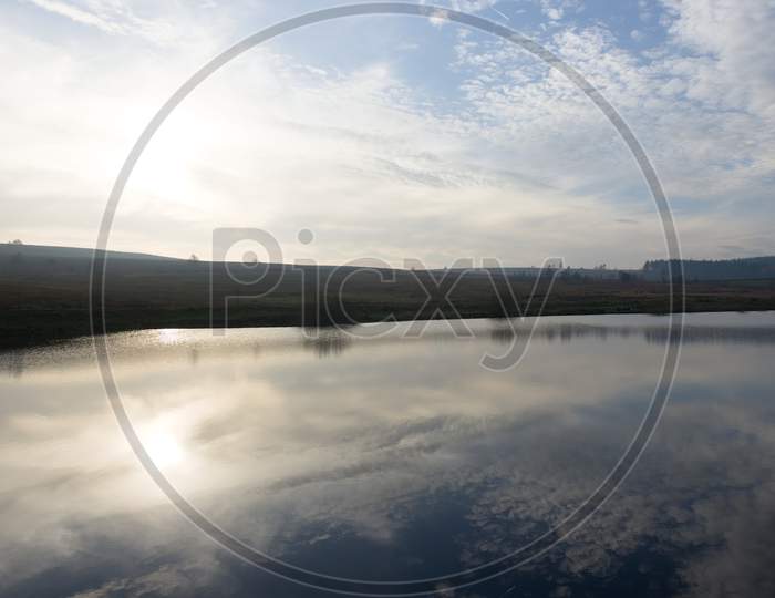 Horizontal Wide Angle Image Of Winters Sky Reflected In Calm Reservoir