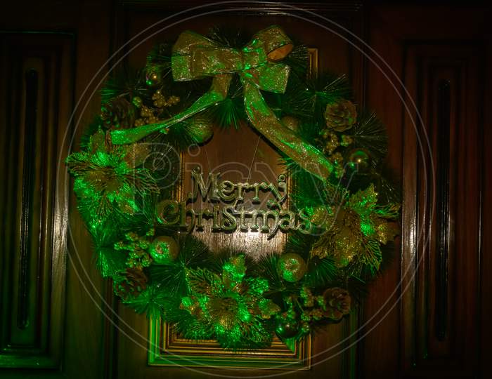 A Decorative Christmas Wreath With Merry Christmas Text On Brown Wooden Door