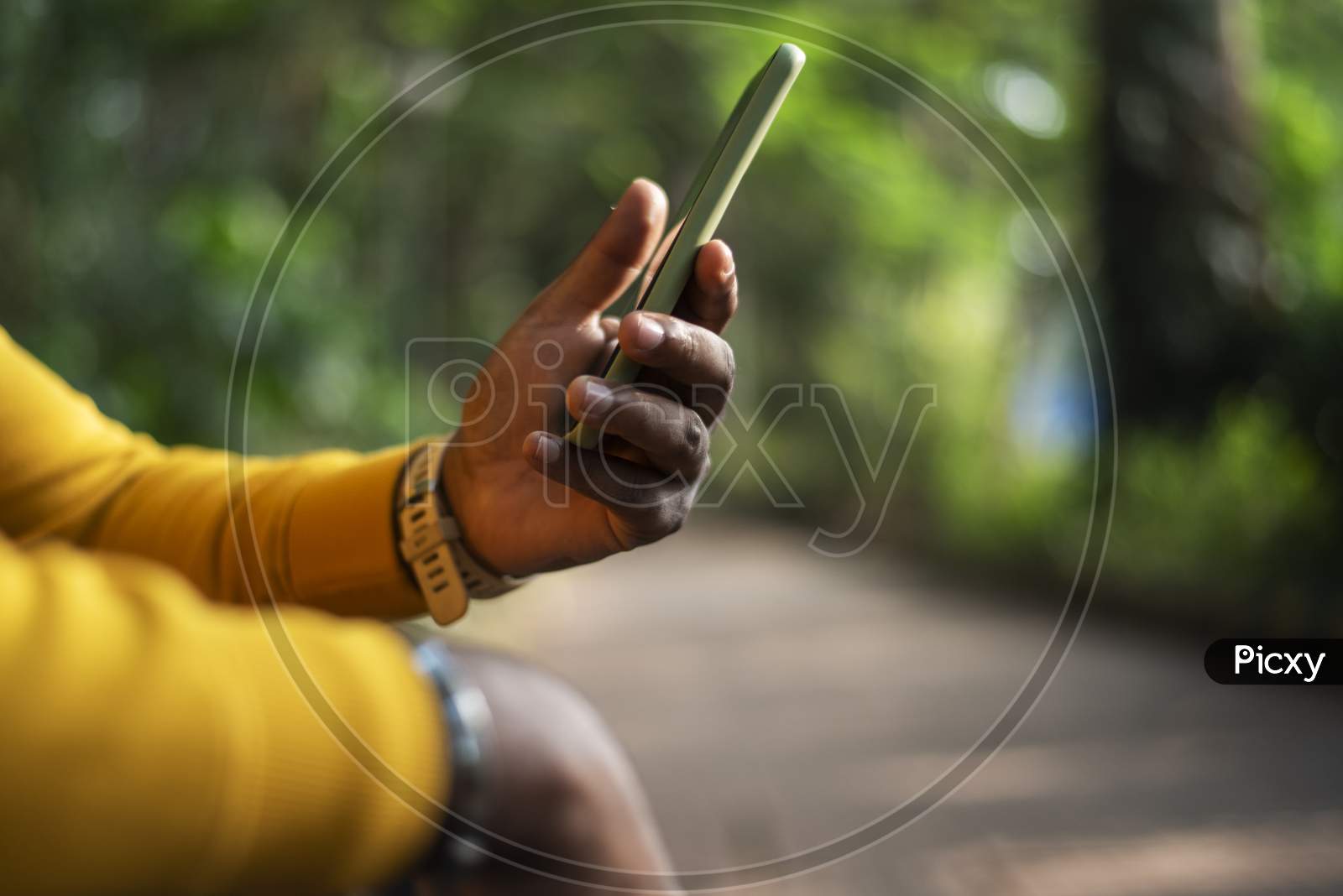 a person using a smartphone on green bokeh background, male hand holding a smartphone