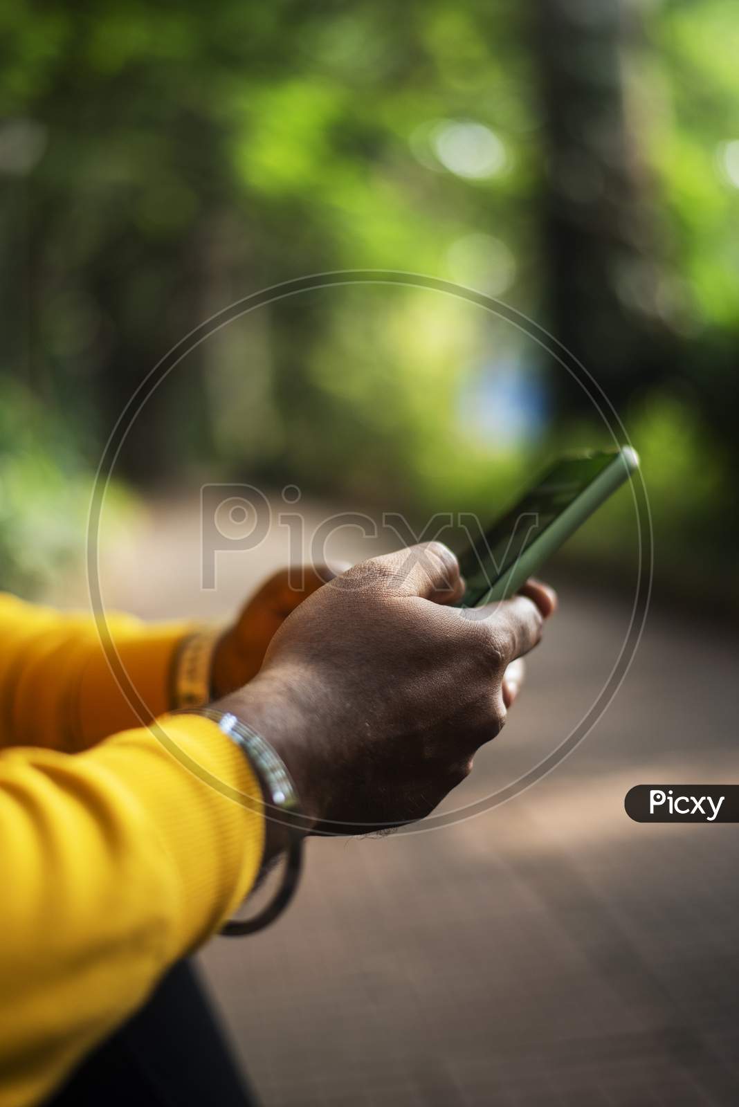 a person using a smartphone on green bokeh background, male hand holding a smartphone