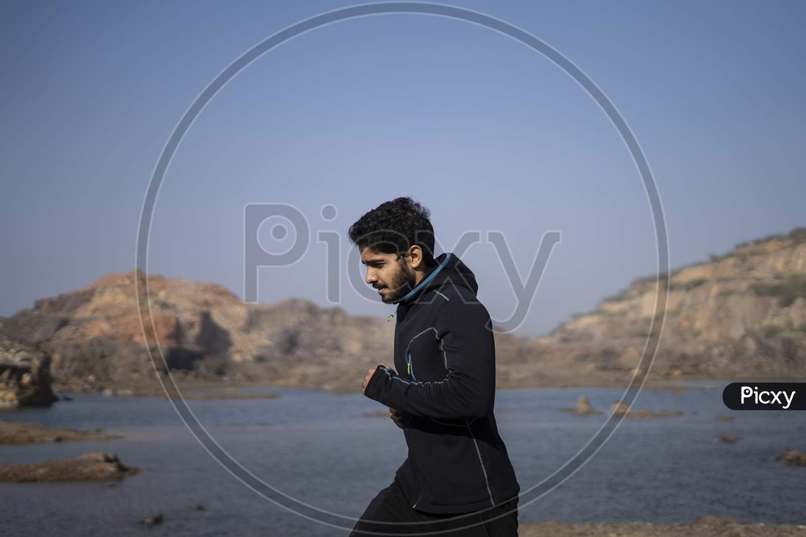 Young Indian Fit Boy Jogging In The Morning Near A Lake Situation In Middle Of A Mountain Area.