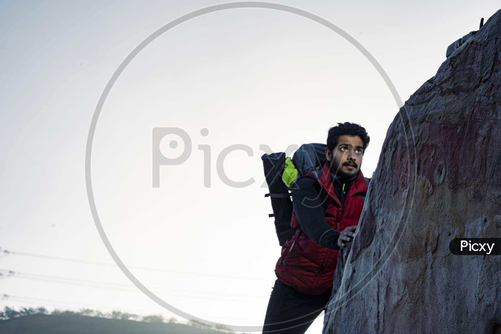Young Indian Climber And Traveler Climbing Up The Mountain Rock During Sunset. Adventure And Sports Concept.
