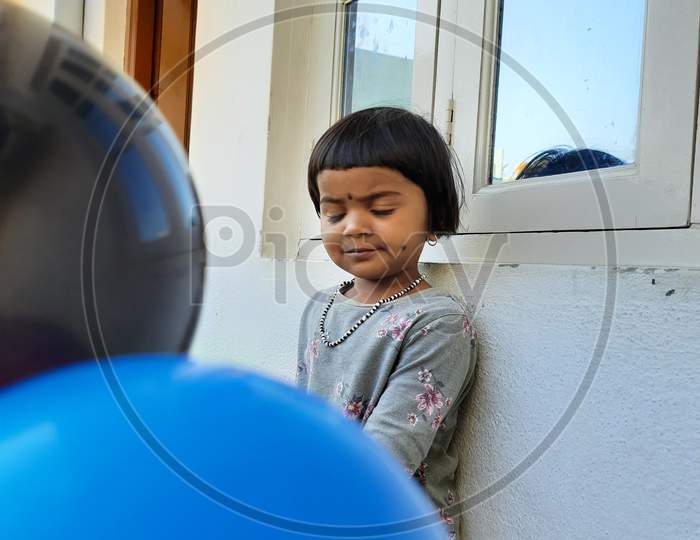 Closeup Of Indian Beautiful Girl Kid Playing With Blue And Black Color Balloon In A Outside Of The House By Blowing