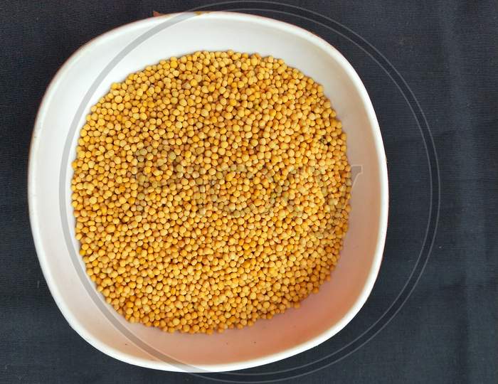 One bowl of yellow mustard seeds with black background