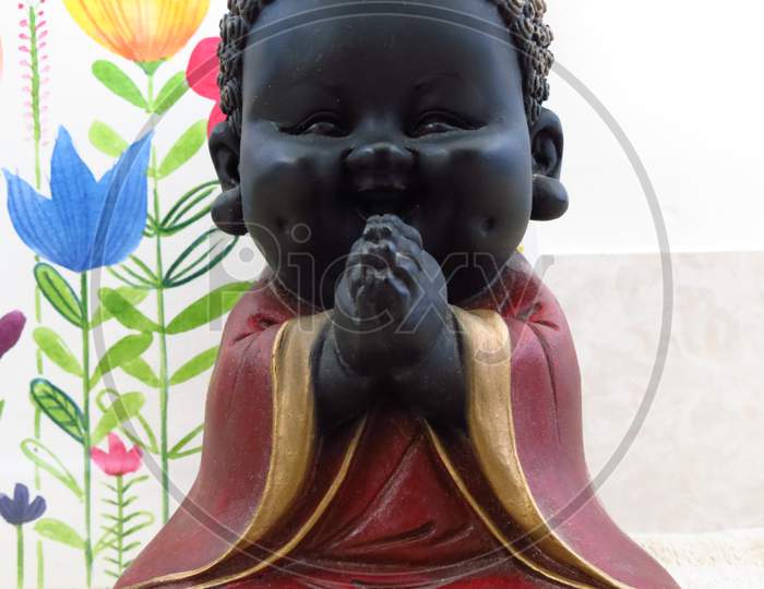 Praying happy Buddha statue with floral background.