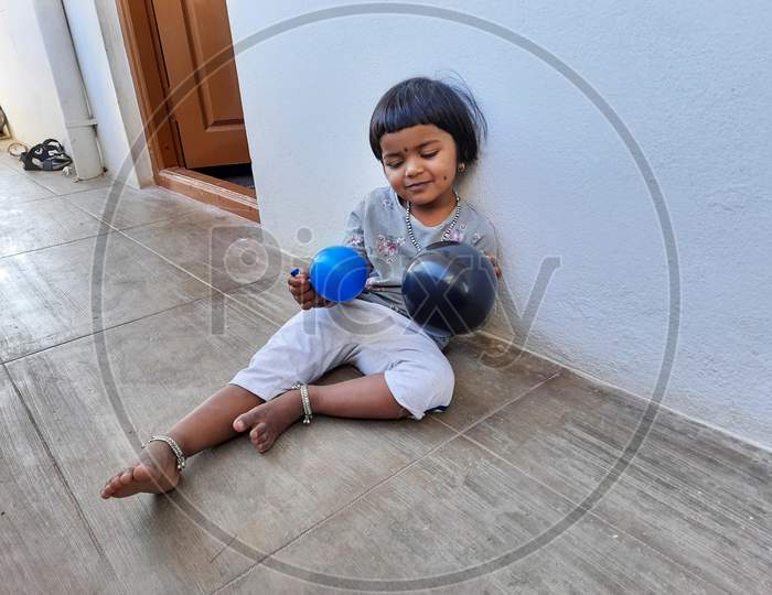 Closeup Of Indian Beautiful Girl Kid Playing With Blue And Black Color Balloon In A Outside Of The House By Blowing