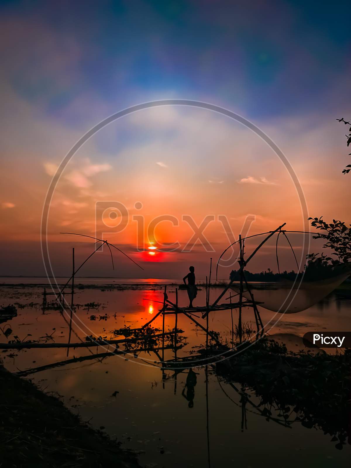 A fisherman in silhouette at sunset, standing on a Chinese Fishing net