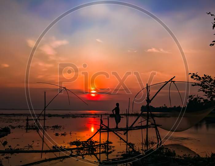 A fisherman in silhouette at sunset, standing on a Chinese Fishing net