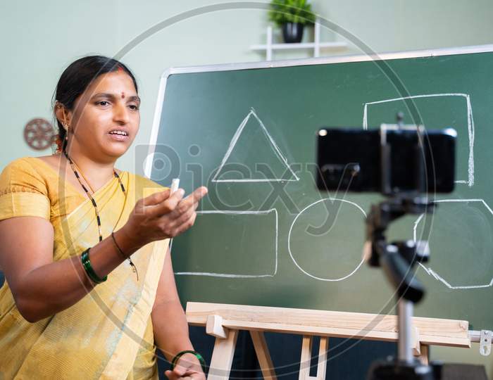 Indian Woman Explaining To Students From Board During Online Class In Front Of Mobile Phone - Concept Of E-Teaching, Remote Learning, Virtual Education During Covid-19 Pandemic