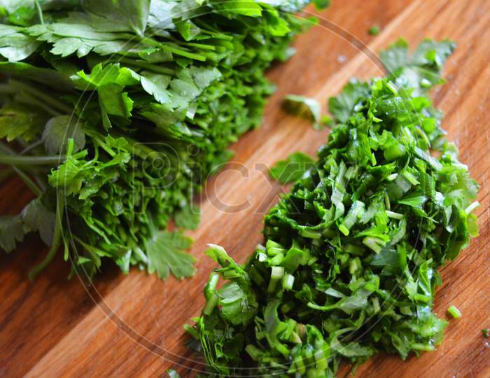 A bunch of green washed fresh parsley and chopped parsley for salad laid out on a wooden kitchen board.