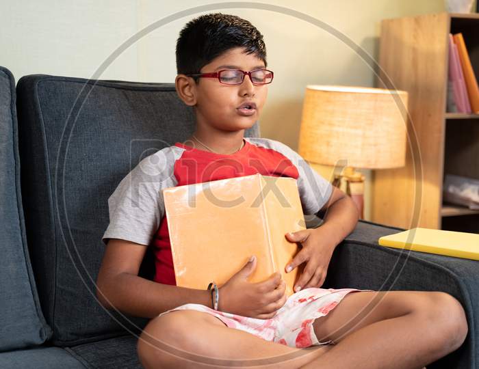 Young Kid Mugging Up Answers From Book During Exams With Out Understanding The Concepts At Home On Sofa - Concept Of Education System And Teenager Kids Lifestyle.