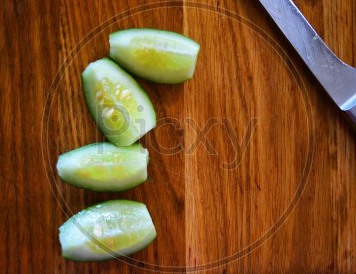 Green fresh sliced cucumbers for a summer salad with a metal kitchen knife lie on a brown wooden kitchen board.