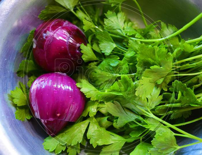 A bunch of wet green washed fresh parsley and purple onions for a salad lined in a gray stainless kitchen toe.