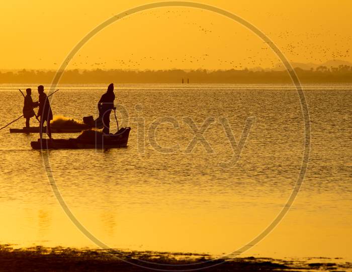 Silhouette View Of The Fishermen With Their Boats In A Lake During Sunset. Selective Focus