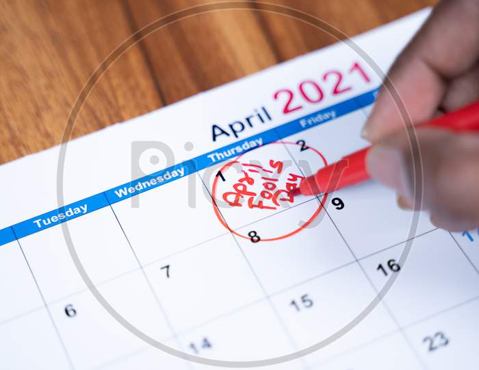 Close Up Hands Writing And Marking April Fools Day On 2021 Calendar.