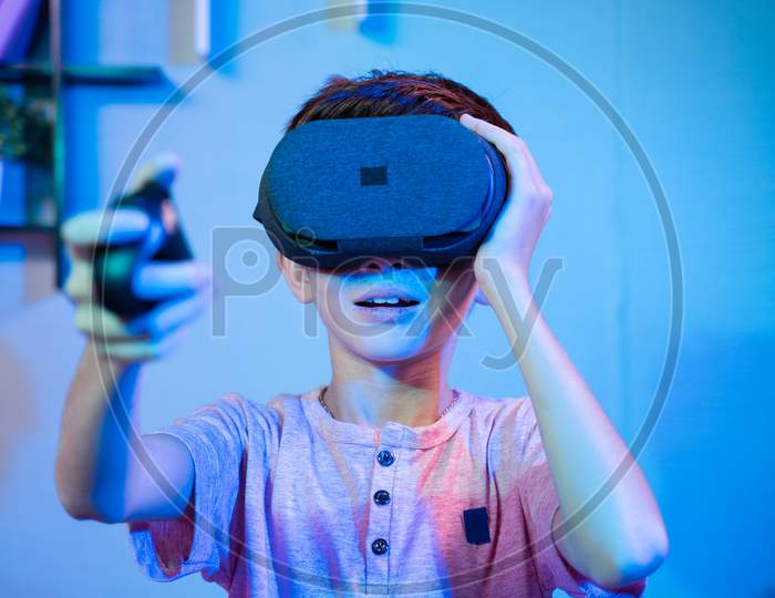 Young Kid Playing Game By Wearing Vr Or Virtual Reality Headset And Game Pad While Sitting On Sofa