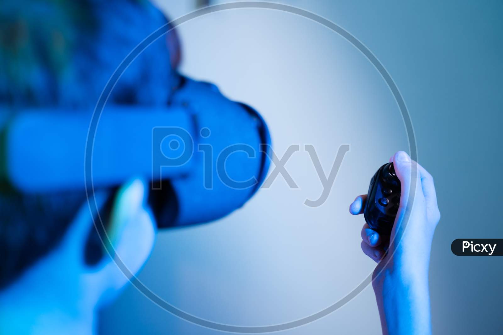 Selective Focus On Joystick, Shoulder Shot Of Kid With Vr Or Virtual Reality Goggles Playing Video Game Using Gampad Or Joystick Showing With Futuristic Lighting Look.