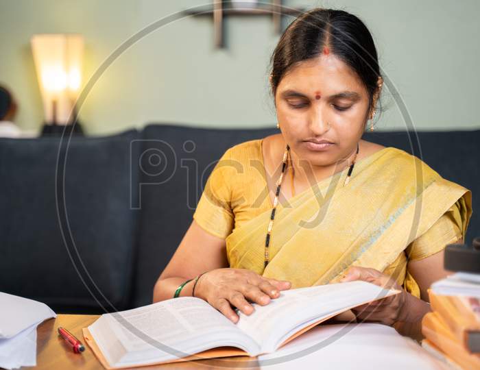 Indian Woman Busy Preparing Form Fom Seeing Books For Teaching Online Class - 40S Lady Studying By Referring Books For Examination At Home.
