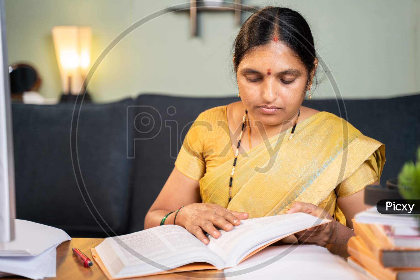 Indian Woman Busy Preparing Form Fom Seeing Books For Teaching Online Class - 40S Lady Studying By Referring Books For Examination At Home.