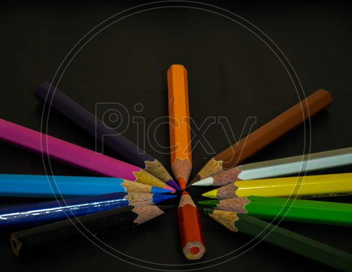 Group Of Color Pencil Crayons Roundly Arranged And Pointing Into Center On Background.